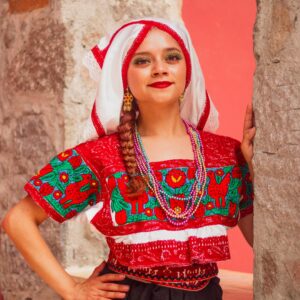 Vibrant portrait of a woman in traditional attire with red and green embroidery, accessorized with beads.