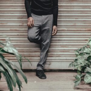 Stylish man posing casually against a roller shutter surrounded by plants.